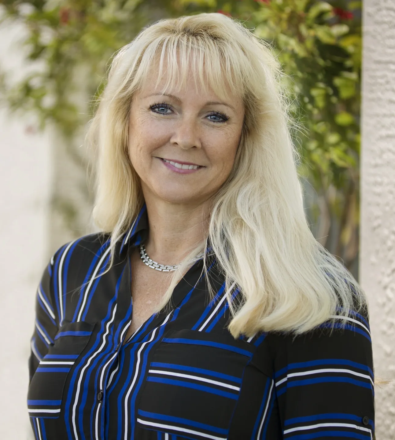 A woman with long blonde hair wearing a blue and black striped shirt.